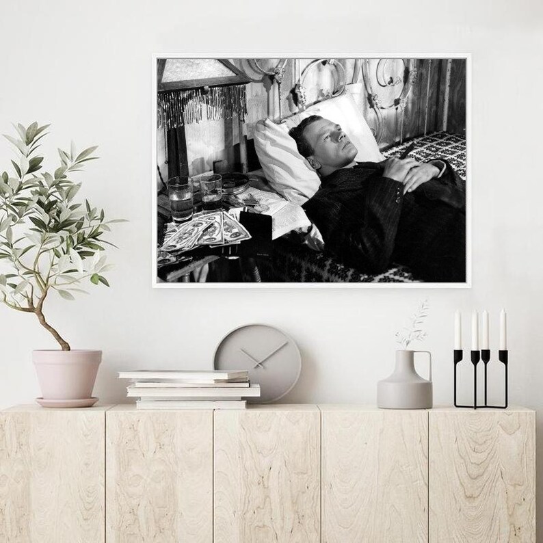 K&ouml;nnte beinhalten: Schwarzwei&szlig;foto eines Mannes, der mit geschlossenen Augen im Bett liegt. Er tr&auml;gt einen Anzug und hat einen ernsten Gesichtsausdruck. Neben ihm stehen Gl&auml;ser und ein Buch auf dem Nachttisch.