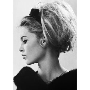 May include: Black and white portrait photograph of a woman with her hair styled in a high bouffant. She is wearing a black fur collar and a thin silver necklace.