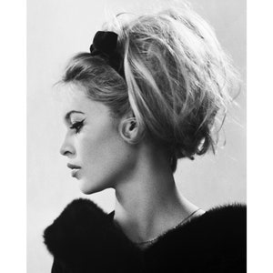 May include: Black and white portrait photograph of a woman with her hair styled in a bouffant. She is wearing a black fur collar and a thin necklace.