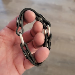 May include: A black leather bracelet with silver metal accents. The bracelet has a chain link design and is adjustable.