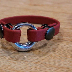 Può includere: Un braccialetto in pelle bordeaux con un anello d'argento al centro con incisa la scritta "Love Always". Il braccialetto è fissato con due chiusure in metallo nero.