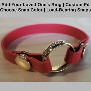 May include: A red leather bracelet with a snap closure. A gold ring with small clear stones is attached to the bracelet.
