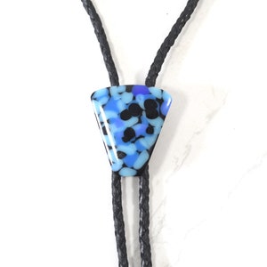 May include: A bolo tie featuring a triangular pendant with a blue, black, and purple speckled design. The pendant is attached to a black braided leather cord, creating a unique accessory. The bolo tie is a stylish addition to any outfit.
