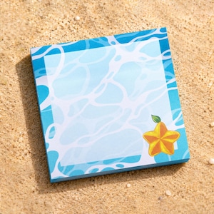 May include: A square notepad featuring a light blue water surface pattern with white ripples and a single yellow starfruit illustration in the bottom right corner. The design includes a wide blue border framing a central area for writing notes.