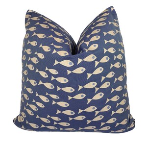 May include: A square cushion featuring a navy blue fabric adorned with a repeating pattern of beige fish. The fish design is stylized and arranged in a flowing pattern. The cushion has a soft appearance, suitable for home decor.