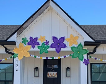May include: A white house with a black roof and black windows. The house is decorated with purple, green, and gold flowers and a string of white, green, and purple beads. The house number is 124. There is a sign on the door that says "AAAA".