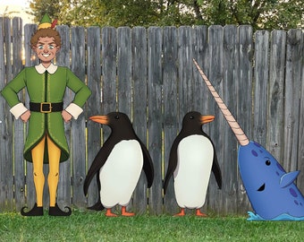 May include: A festive Christmas yard display featuring a snowman wearing sunglasses and a tie, a green elf with a pointed hat, two penguins, and a blue narwhal. A red sign reads "There's Room for Everyone on the Nice List".