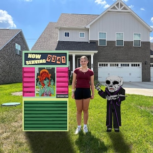 May include: A green and pink sign with the text "NOW SERVING 9341" and the word "INFORMATION" on the bottom. A woman in a red shirt and black shorts stands in front of the sign. A black and white monster with a purple robe and a knife stands in the grass.