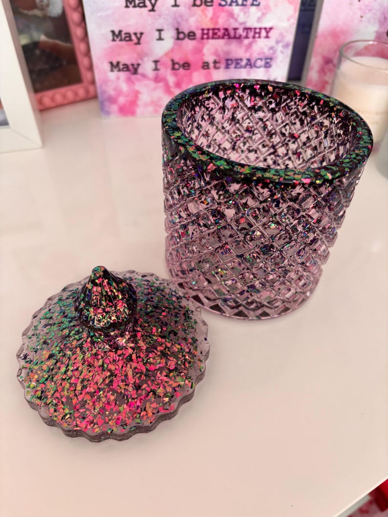 K&ouml;nnte beinhalten: Ein rosa Glasgef&auml;&szlig; mit Deckel, beide mit schimmerndem Glitzer verziert. Das Gef&auml;&szlig; hat ein Diamantenmuster und einen schwarzen Rand. Der Deckel hat eine spitze Oberseite.
