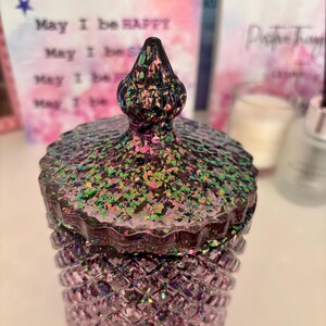 K&ouml;nnte beinhalten: Eine lilafarbene Glasdose mit einem regenbogenfarbenen Glitzerdeckel. Die Dose hat ein Diamantenmuster und der Deckel hat eine spitze Spitze.