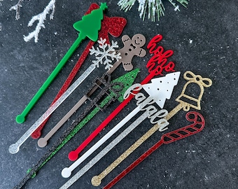 May include: Set of 10 Christmas-themed cocktail stirrers with glitter accents. The stirrers feature various designs, including a Christmas tree, a gingerbread man, a snowflake, a bell, a candy cane, and the words "Ho Ho Ho" and "Jingle All The Way".