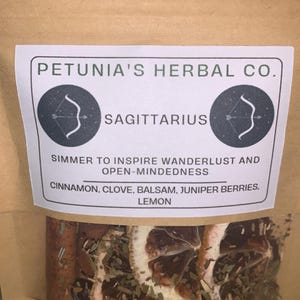 May include: A brown paper bag with a white label that says "PETUNIA'S HERBAL CO." and "SAGITTARIUS". The label also says "SIMMER TO INSPIRE WANDERLUST AND OPEN-MINDEDNESS" and lists the ingredients: "CINNAMON, CLOVE, BALSAM, JUNIPER BERRIES, LEMON". The bag contains dried herbs and fruit.