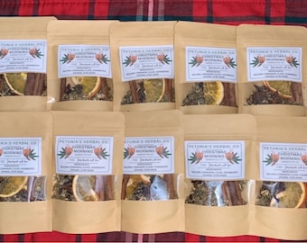 Puede incluir: Diez pequeñas bolsas de papel marrón con ventanas de plástico transparente, cada una contiene una mezcla de hierbas secas, especias y frutas. Las bolsas están etiquetadas "Petunia's Herbal Co. Christmas Morning" y enumeran los ingredientes: "Canela molida, clavo, naranja, anís estrellado".
