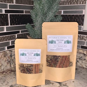 May include: Two brown paper bags with a white label that reads "Petunia's Herbal Co. Balsam Tree Simmer Pot Kit". The bags contain dried herbs and spices, including cinnamon sticks, star anise, and cloves. The bags are sitting on a brown countertop.