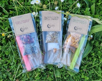 May include: Three small clear plastic bags each containing a spell jar kit. The bags are labeled "Love Thyself Spell Jar Kit", "Protection Spell Jar Kit", and "Abundance Spell Jar Kit". Each kit contains a small glass jar, herbs, and a candle.