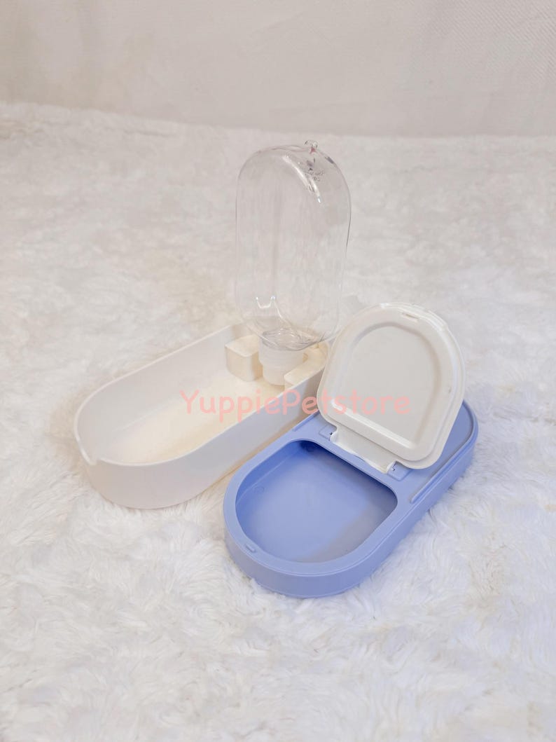 K&ouml;nnte beinhalten: Ein wei&szlig;-blauer Wasserspender und Futternapf f&uuml;r Haustiere. Der Spender hat eine transparente Wasserflasche, ein wei&szlig;es Futtertablett und eine blaue Wasserschale. Die Wasserschale hat einen wei&szlig;en Deckel.