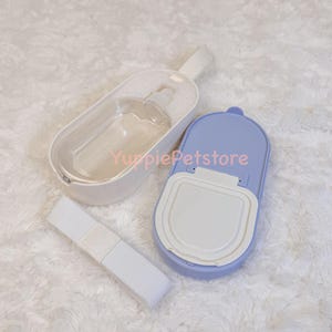 K&ouml;nnte beinhalten: Ein Reise-Set f&uuml;r Haustiere mit einer transparenten Wasserflasche in einem wei&szlig;en Halter, einem hellvioletten Futterbeh&auml;lter und einem wei&szlig;en Gurt. Das Set ist f&uuml;r Reisen mit Haustieren konzipiert.