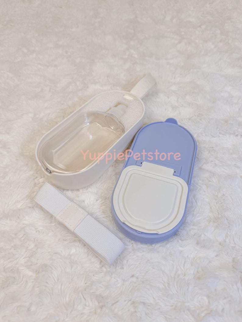 K&ouml;nnte beinhalten: Ein Reise-Set f&uuml;r Haustiere mit einer transparenten Wasserflasche in einem wei&szlig;en Halter, einem hellvioletten Futterbeh&auml;lter und einem wei&szlig;en Gurt. Das Set ist f&uuml;r Reisen mit Haustieren konzipiert.