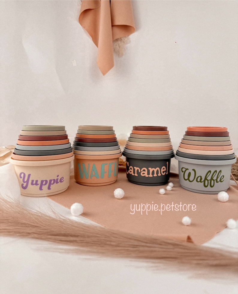 May include: Set of four stackable silicone nesting bowls in various shades of brown, gray, and beige. The bowls are labeled "Waffle", "Caramel", "Waffle", and "Yuppie".