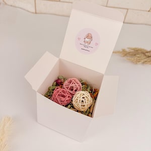 May include: A white box, lid open, displaying pink and beige woven balls amongst dried herbs and flowers. The box has a circular sticker with a cartoon bunny and the text "people petstore".