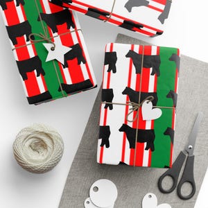 May include: Gift-wrapped presents with black cow print wrapping paper, red and white stripes, and green accents. The gifts are tied with twine and adorned with star and heart-shaped tags. A ball of twine and scissors are also visible.