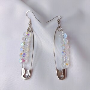 May include: A pair of silver safety pin earrings with iridescent crystal beads. The earrings are dangling and have a simple design.