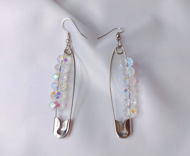 May include: A pair of silver safety pin earrings with iridescent crystal beads. The earrings are dangling and have a simple design.