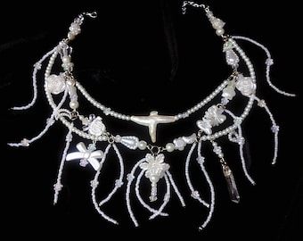 May include: A white pearl necklace with multiple strands and various charms, including flowers, a bow, and a crystal pendant.