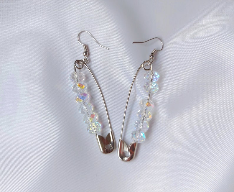 May include: A pair of silver safety pin earrings with clear iridescent crystal beads.