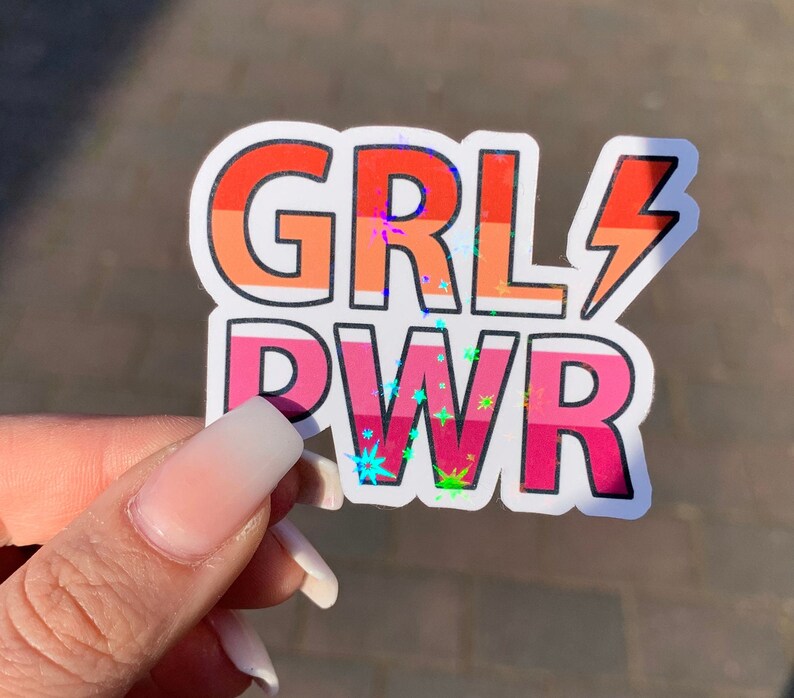 Puede incluir: Una pegatina con las palabras "GRL PWR" en colores arco&iacute;ris con un acabado hologr&aacute;fico. La pegatina tiene un dise&ntilde;o de rayo.