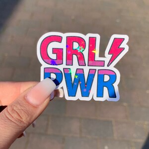 Puede incluir: Una pegatina con el texto "GRL PWR" en rosa y azul con un rayo y estrellas de purpurina.