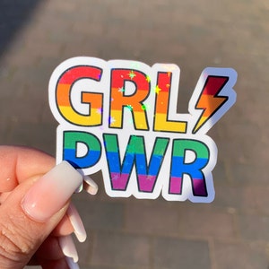 Puede incluir: Una pegatina de arco&iacute;ris con el texto "GRL PWR" y un rayo. La pegatina tiene un acabado hologr&aacute;fico.