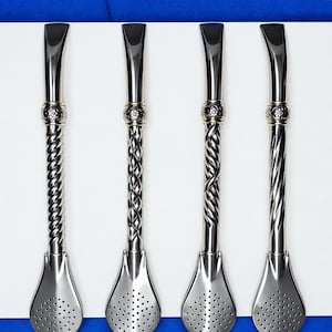 Puede incluir: Cuatro pajitas bombilla de metal plateado para mate, cada una con un tallo largo y delgado con distintos patrones trenzados o retorcidos, una banda floral decorativa cerca de la parte superior y una base de filtro plana y perforada.