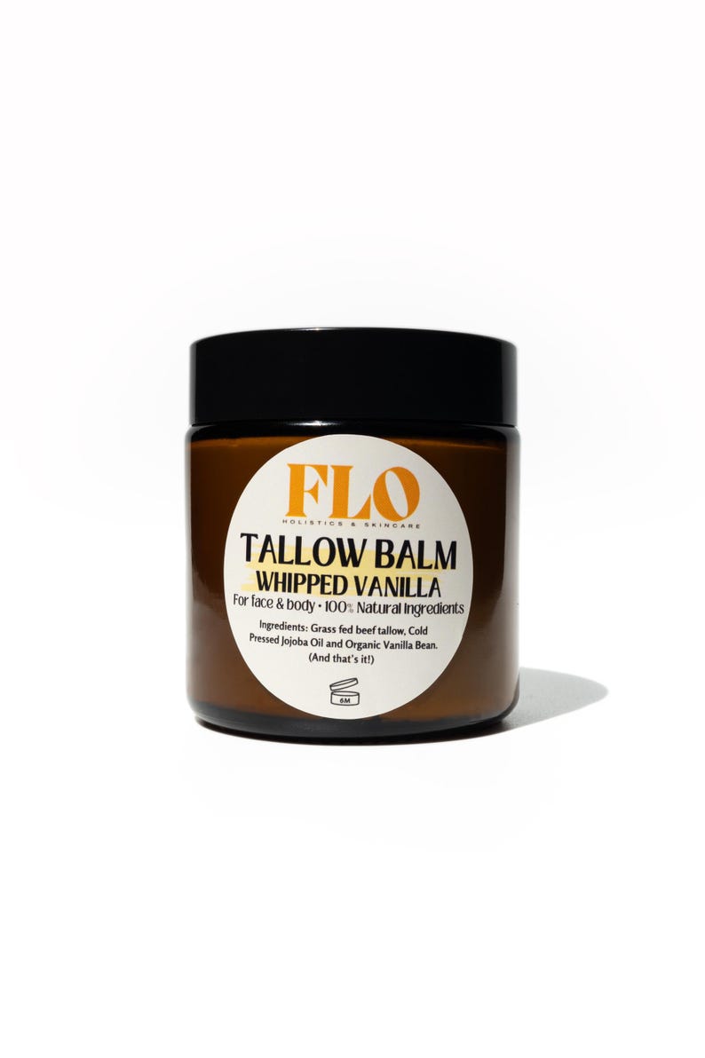 Op de afbeelding: Een bruine pot met een zwart deksel, met het opschrift "TALLOW BALM WHIPPED VANILLA" met het FLO Holistic & Skincare logo. De tekst geeft aan dat het voor gezicht en lichaam is, gemaakt met natuurlijke ingredi&euml;nten.