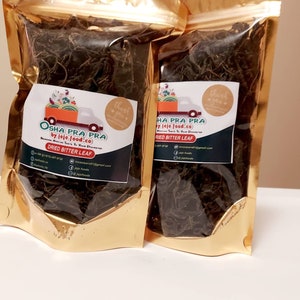 May include: Two gold foil pouches filled with dried bitter leaf. Each pouch has a label with the text "OSHA PRA PRA" and "DRIED BITTER LEAF". The labels also feature a graphic of a truck carrying produce and the words "thank you".