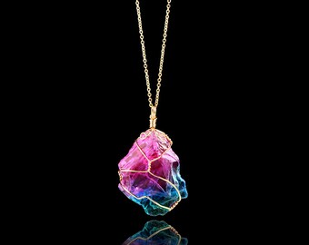 May include: A gold chain necklace with a large, iridescent crystal pendant. The crystal is wrapped in gold wire and has a gradient of pink, purple, and blue colors.