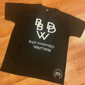 Könnte beinhalten: Schwarzes T-Shirt mit weißem Text, der "BBW Back Door Vibes Trust None" lautet, und einem weißen Kreislogo, auf dem "Back Door Vibes" steht, mit den Buchstaben "BDV" im Kreis.