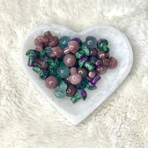 May include: A heart-shaped white dish filled with small, polished gemstone mushrooms in shades of green, pink, and blue.