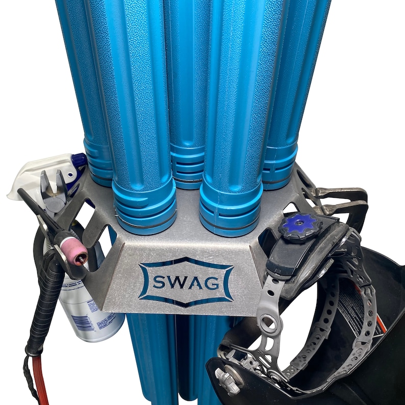 May include: A metal welding rod holder with the word "SWAG" engraved on the front. The holder has eight slots for welding rods and a space for a welding helmet. The holder is made of metal and has a silver finish.