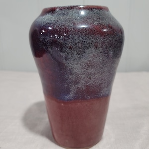 Puede incluir: Un pequeño jarrón de cerámica hecho a mano con un esmalte moteado en tonos de morado, marrón y blanco.