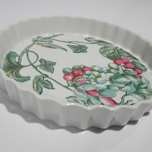 Peut inclure: Plat à four en céramique blanche avec un bord festonné. Le plat présente un motif peint de vignes de raisin vertes avec des raisins roses et verts.