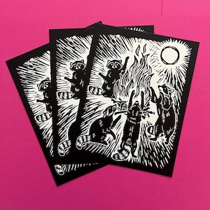 Könnte beinhalten: Schwarz-weißer Linolschnitt von fünf Waschbären, die um ein Lagerfeuer versammelt sind. Die Waschbären sind vor einem weißen Hintergrund mit einer Sonne oben rechts silhouettiert.