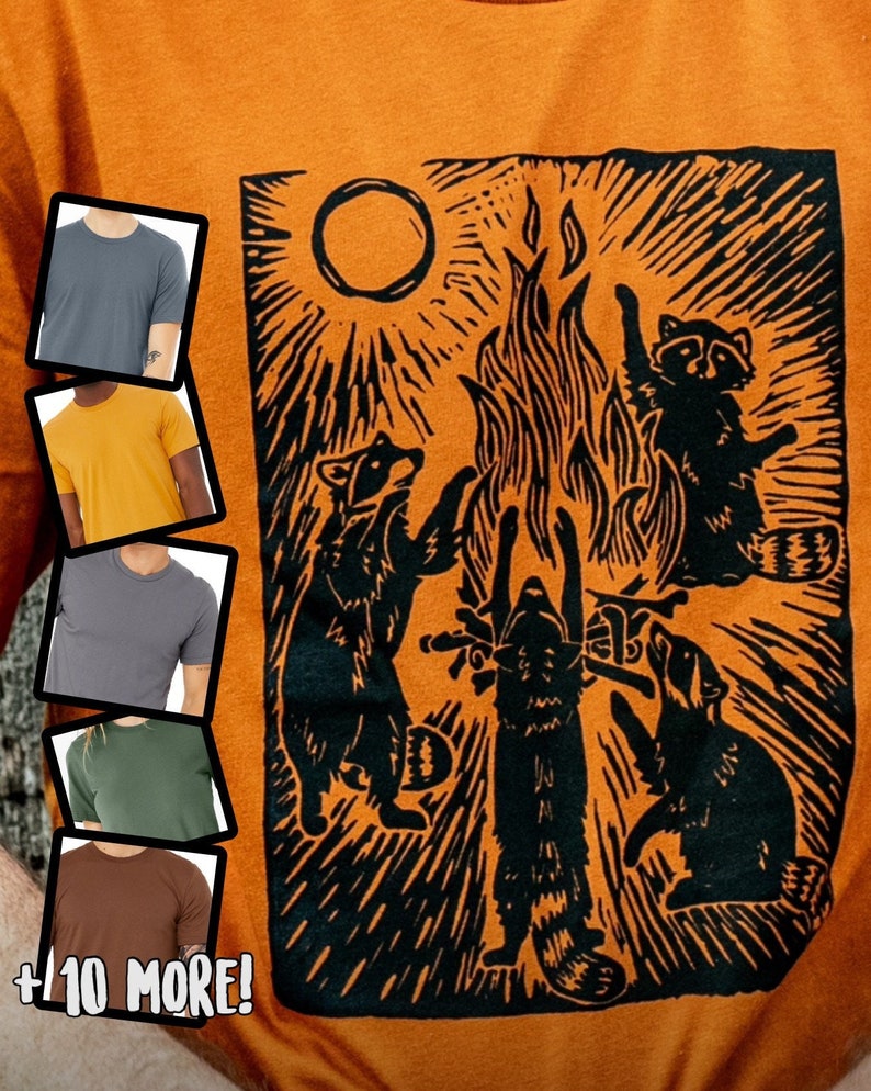 Pu&ograve; includere: Maglietta arancione con un'illustrazione in bianco e nero di quattro procioni attorno a un fal&ograve;. L'illustrazione &egrave; in stile xilografia. Il testo " +10 MORE!" &egrave; nella parte inferiore dell'immagine.