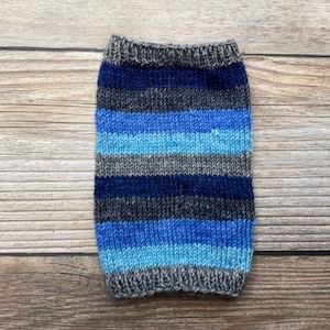 May include: A knitted pet sweater in shades of blue, gray, and navy. The sweater features horizontal stripes and a ribbed collar and hem. The item is designed to fit a small dog or cat, providing warmth and style.