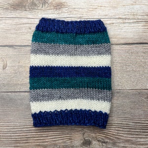 May include: A knitted dog sweater with horizontal stripes in shades of blue, teal, gray, and white. The sweater is made of a soft yarn and has a ribbed collar and hem. The garment is designed to fit a small dog.