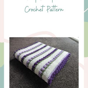 Peut inclure: Une couverture crochetée avec un motif rayé blanc, violet et vert. La couverture a un bord festonné et le texte "Tulip Blanket Crochet Pattern" en écriture cursive.