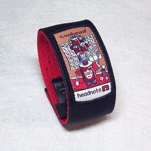 May include: A black and red wristband with a colorful patch featuring a cartoon character and the text "canhead headnots".