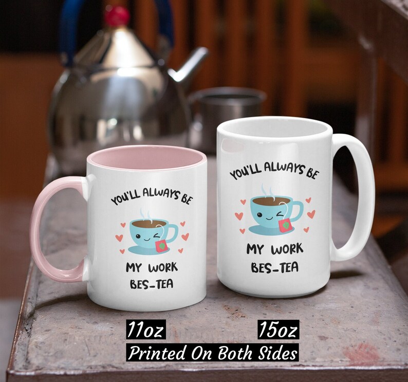 May include: Two white ceramic mugs with pink and blue accents. The mugs feature a cartoon teacup with a smiling face and the text "You'll always be my work bes-tea". The smaller mug is 11 ounces and the larger mug is 15 ounces.