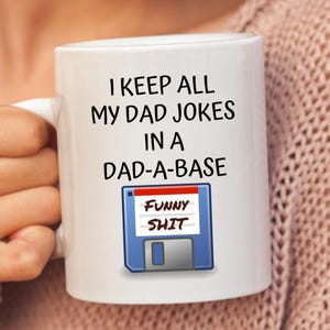 May include: White ceramic mug with the text "I keep all my dad jokes in a dad-a-base" and a floppy disk icon with the text "Funny Shit" on it.