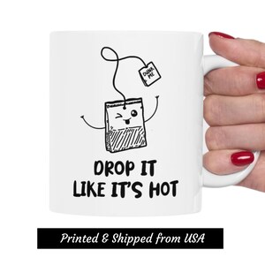 May include: White ceramic mug with a black and white illustration of a tea bag with a face and the text "Dunk Me" on a tag. The text "Drop It Like It's Hot" is printed below the illustration.